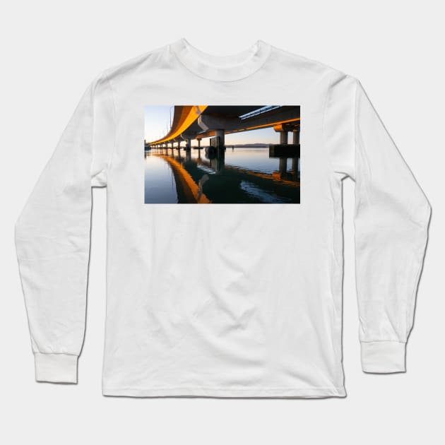 Morning sun strikes side Tauranga Harbour Bridge in golden hue reflected leading lines into calm water below Long Sleeve T-Shirt by brians101
